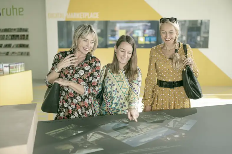 Drei Frauen bedienen einen interaktiven digitalen Tisch. Bild: KTG Karlsruhe Tourismus GmbH